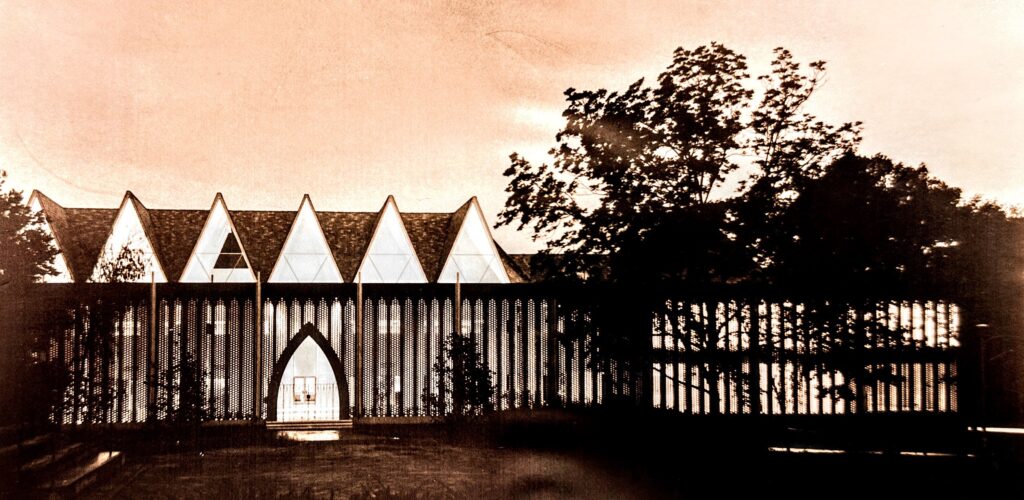 photograph of Dana Fine Arts Building from the front, includes three triangular windows on second level, brick exterior wall and pointed arch gateway. Taken in evening light