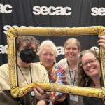 (l-r) August Fisk '25, Nell Ruby, Tallulah Stroud '26, Katherine Smith in front of secac step and repeat photo banner holding an inflatable gilded frame