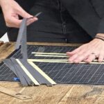 close up of two white hands with strips of paper beginning the process of weaving on a table top