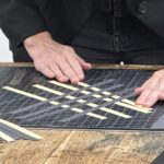close up of two white hands with strips of paper in the process of weaving on a table top