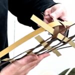 Jess Jones demonstrates the folding of a simple weaving of three colors of paper strips laid in three directions on a table top