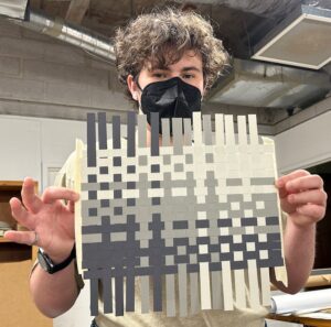 August Fisk holds up a black white and grey weaving of paper