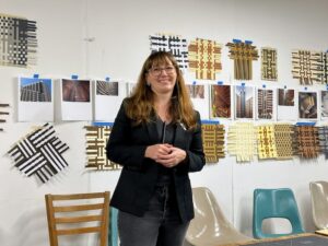 Visiting artist Jess Jones stands in front of a wall of completed weavings from the workshop